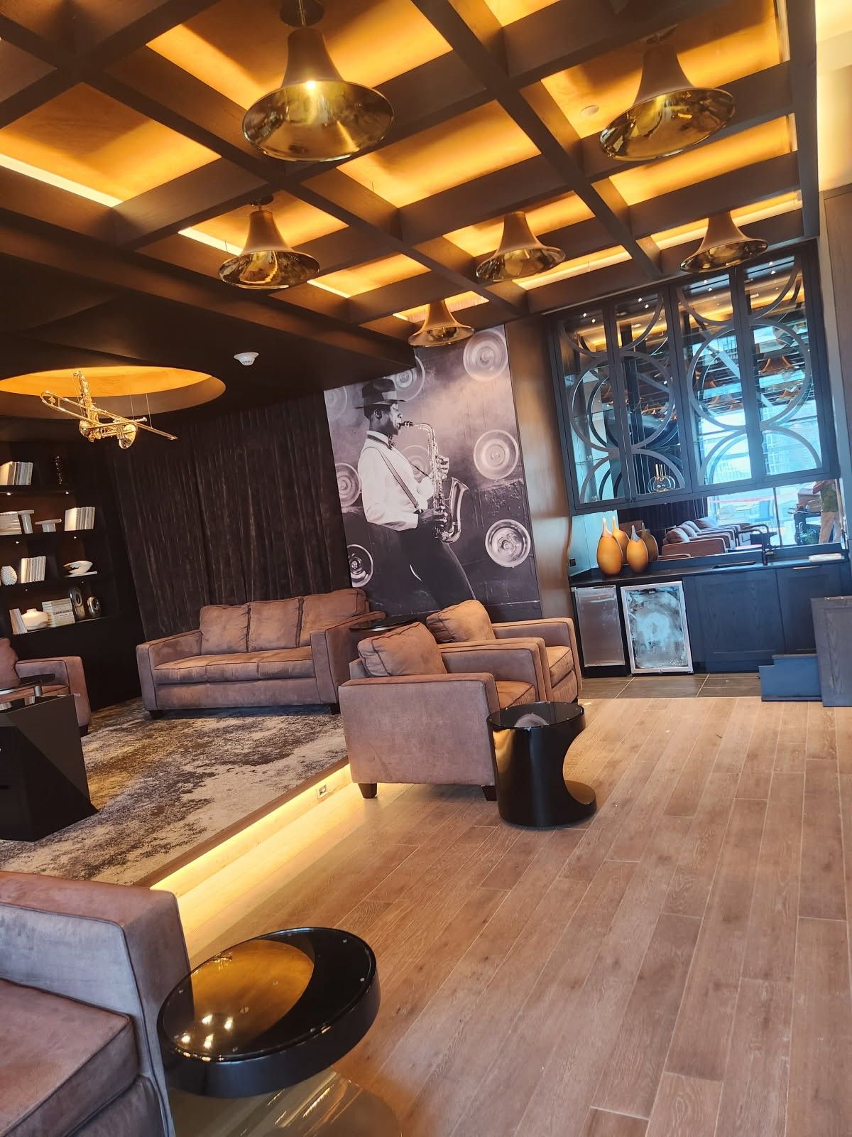 Warm modern lounge with wooden ceiling, gray seating, and decorative wall art under ambient lighting