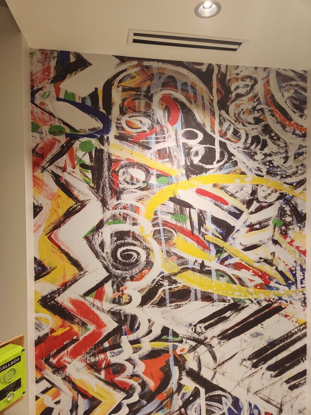 Abstract graffiti-style mural with bold black, white, red, yellow, and green zigzags and spirals on a wall