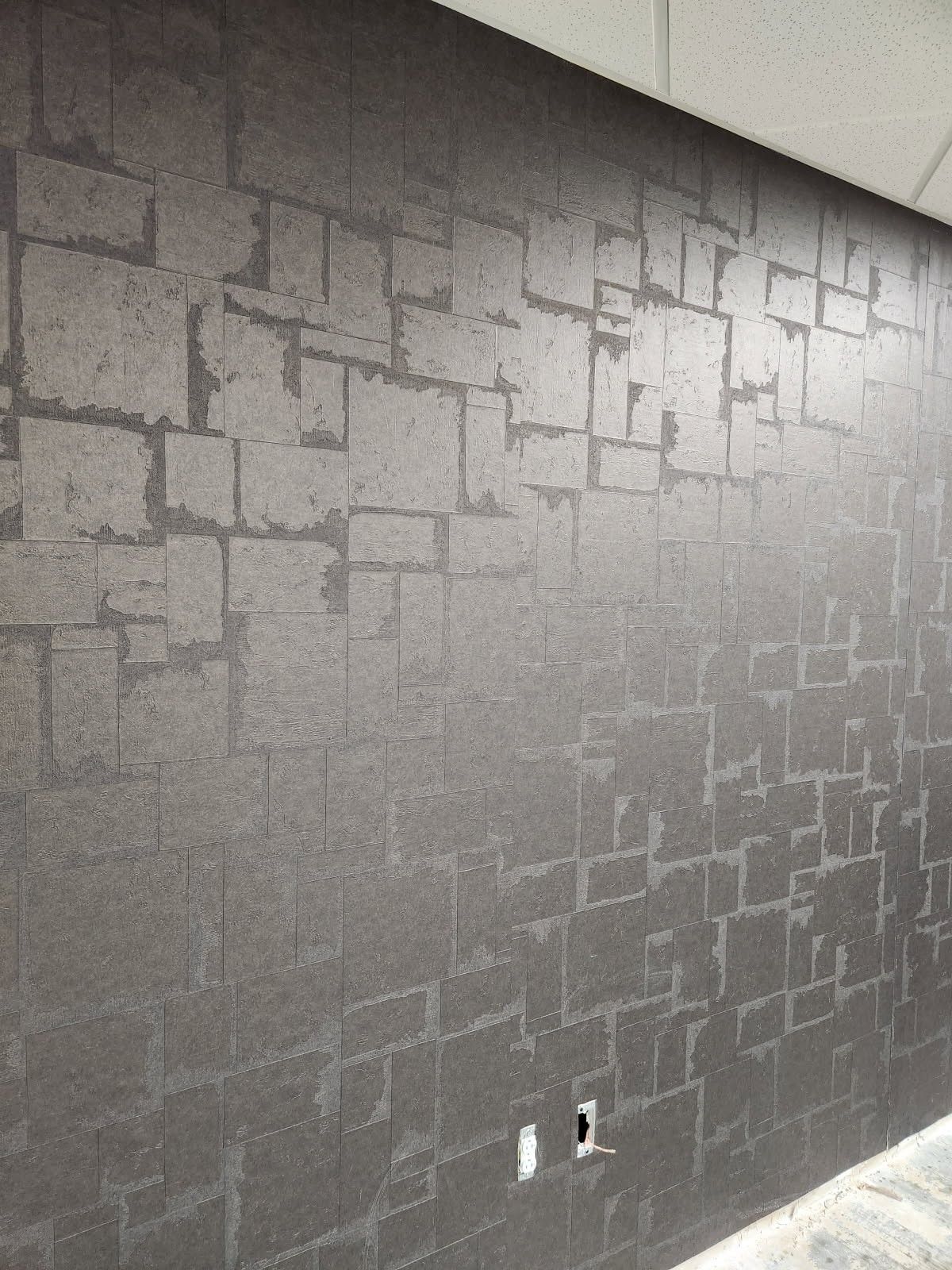 Gray textured wall with a subtle block pattern and two electrical outlets near the bottom.