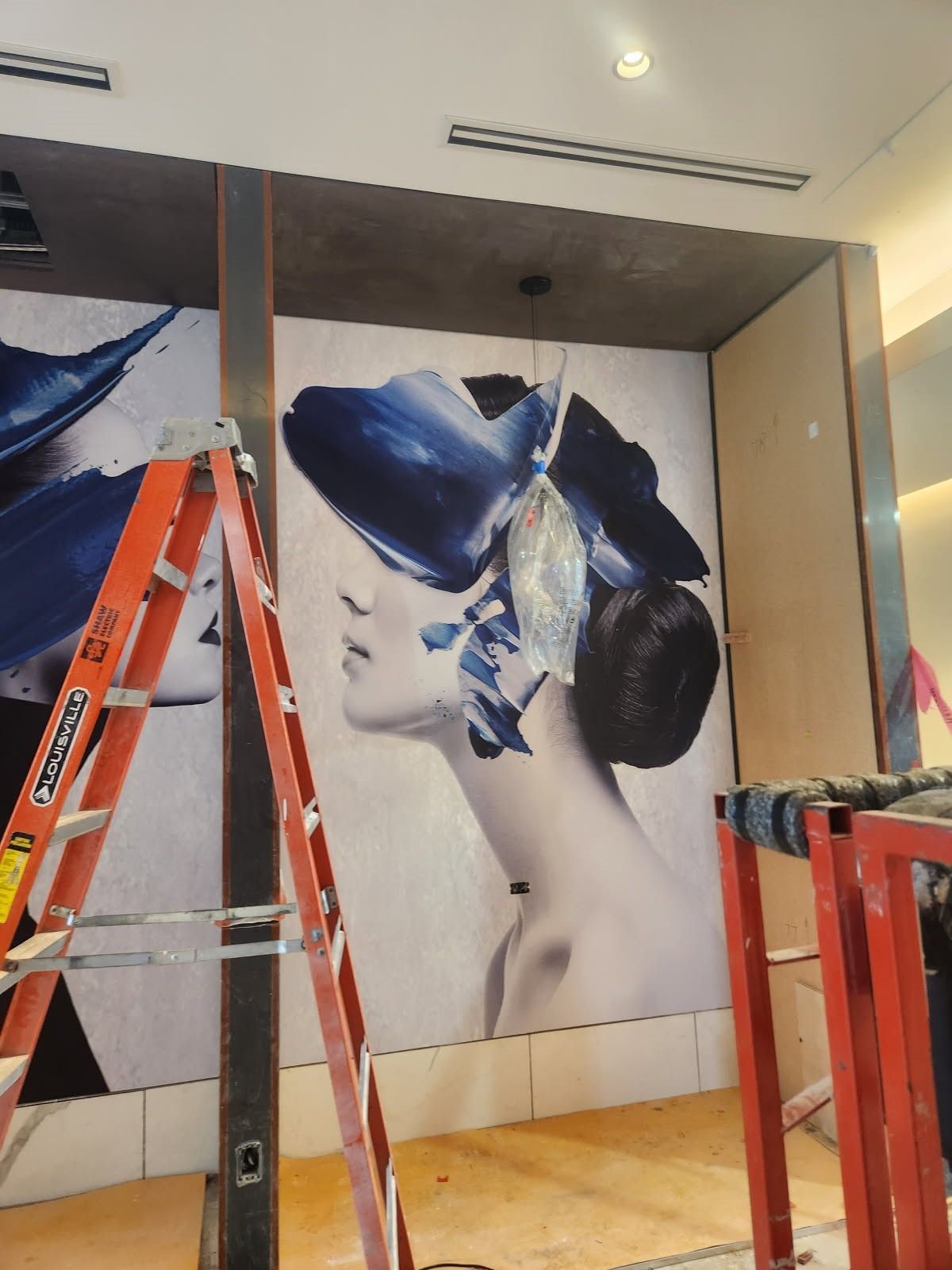 Large wall mural of a woman in profile with a blue butterfly headpiece, installed in a room under construction.