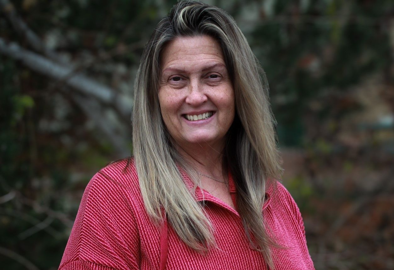 Smiling woman in a red patterned shirt standing outdoors against a blurred background