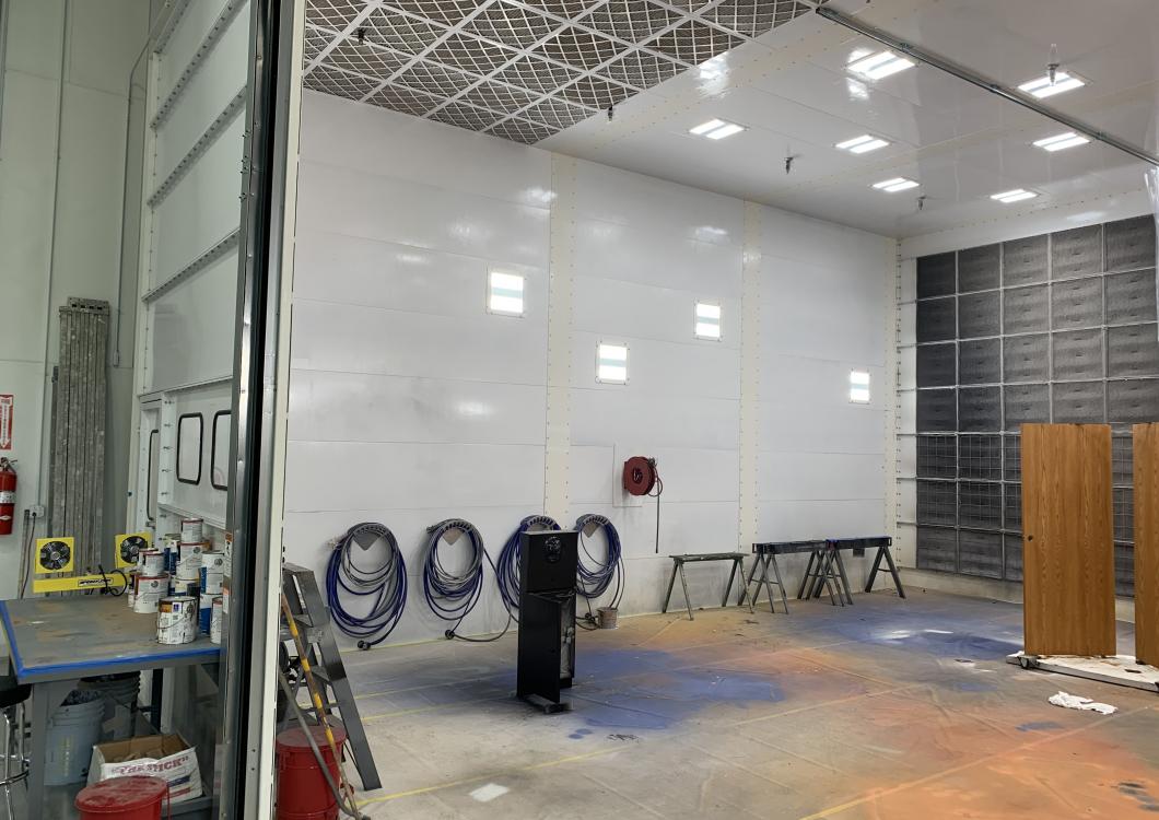 Empty auto shop interior with white walls, tires stacked on the floor, and wooden cabinets on the right