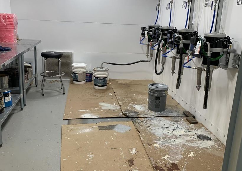 Tidy workshop room with paint-splattered floor, paint cans, and spray guns mounted on the wall