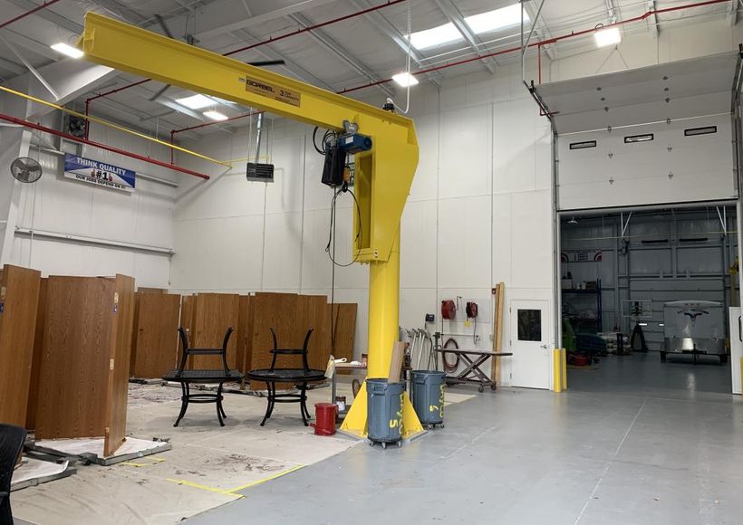 Yellow industrial crane in a warehouse with stacked tables and chairs nearby