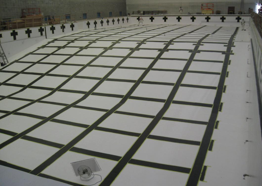 Large indoor space with a grid of white and dark rectangular panels on the floor, viewed from above