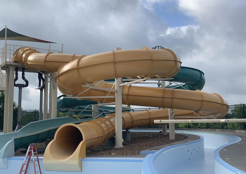 Outdoor water slide complex with tan and teal enclosed slides against a cloudy sky