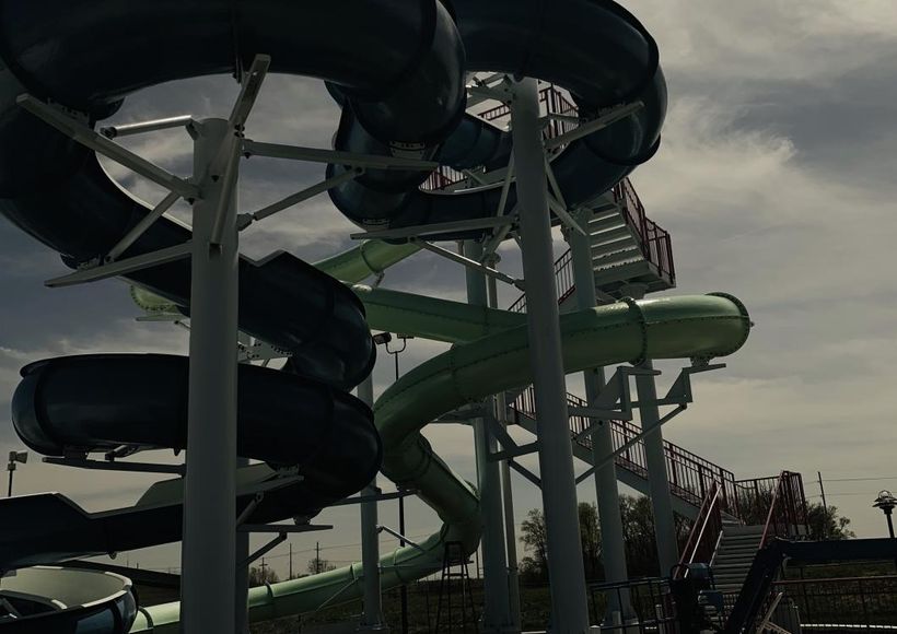 Tall green and black water slides against a cloudy sky at an amusement park