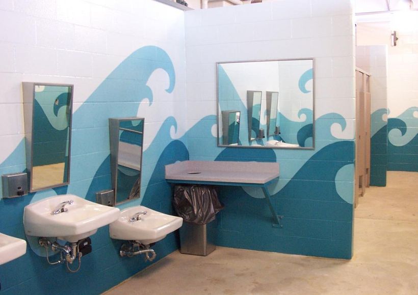 Accessible bathroom with blue wave wall mural, sinks, mirrors, and a wheelchair-accessible counter.