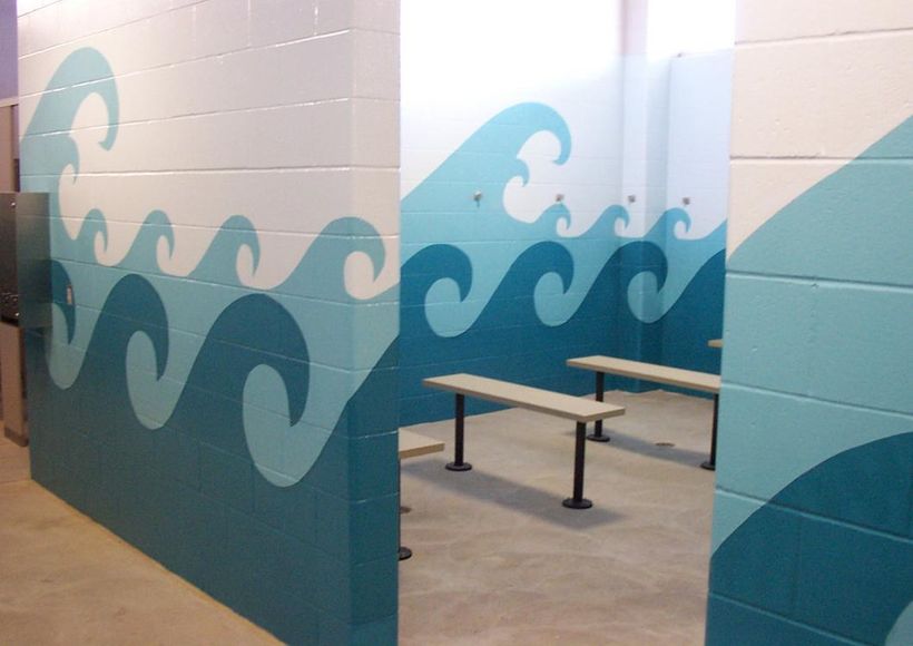 Blue wave mural on tiled walls surrounding a small room with benches and a concrete floor