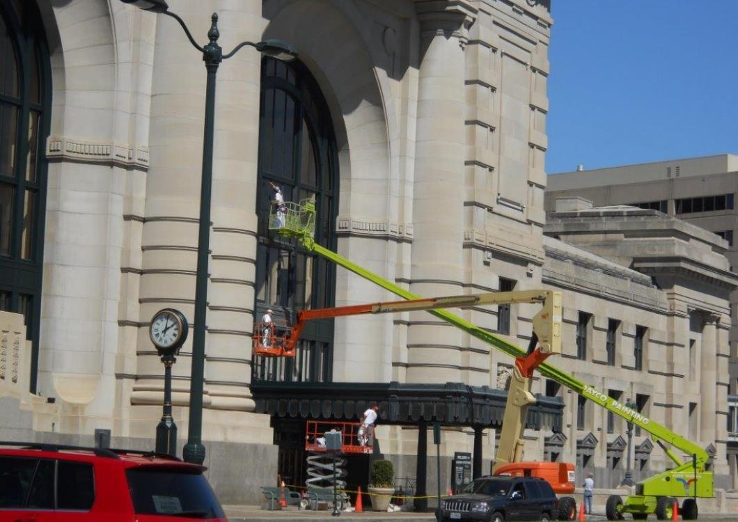 Large stone building with a green boom lift reaching up to a window.