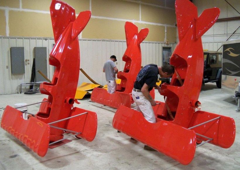 Three bright red industrial machines in a workshop, with two people inspecting them