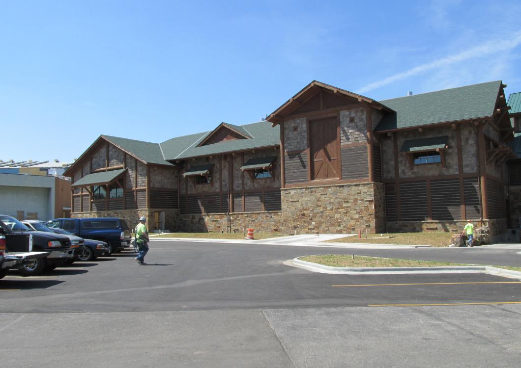 Wide view of a rustic stone building with green roof in a parking lot on a sunny day