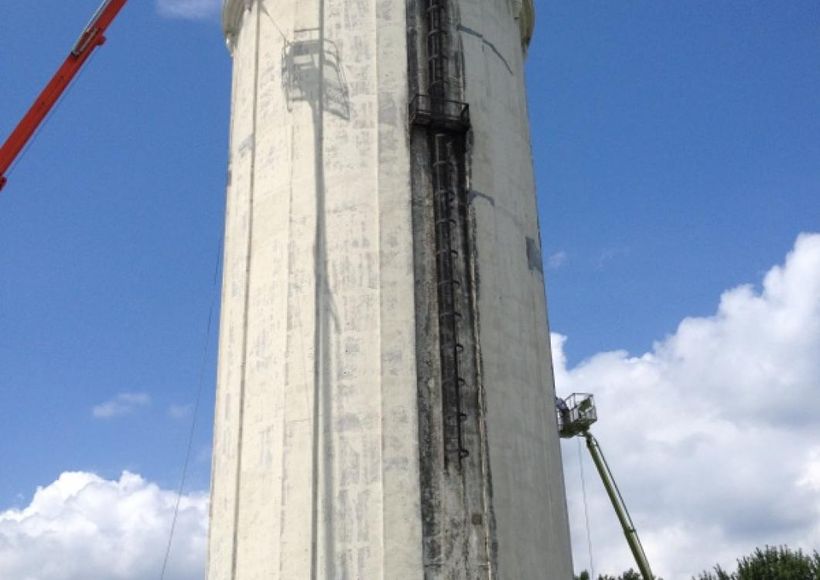 Concrete tower under construction with dark streaks, against a blue sky with clouds