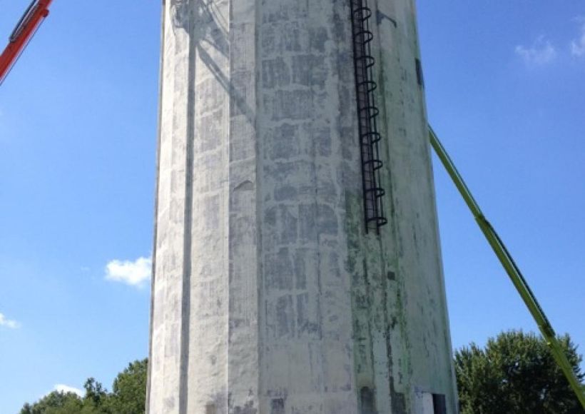 Large concrete tower under construction against a blue sky, with cranes and support beams visible.