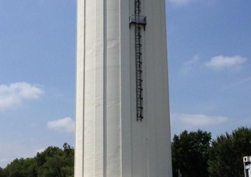 White water tower against a blue sky with trees below