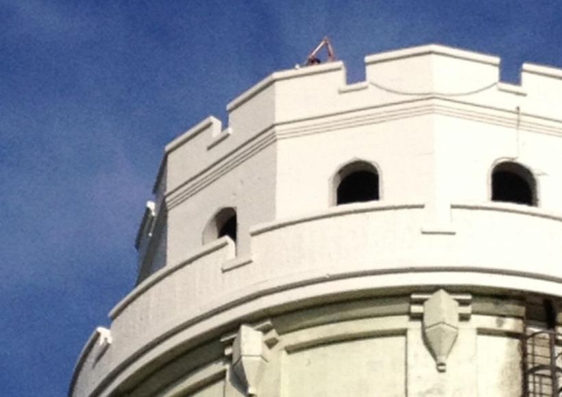 White stone tower against a blue sky, with arched windows and a curved parapet.