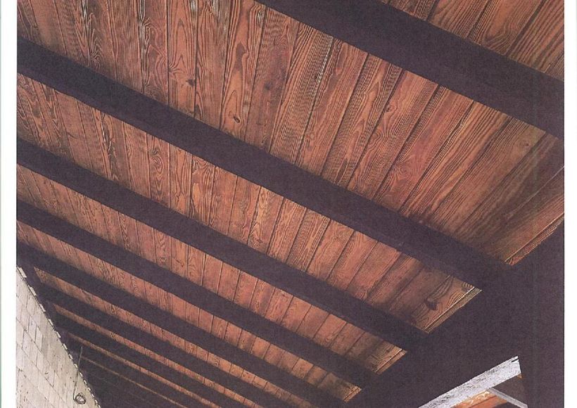 Wooden ceiling with dark exposed beams and textured brown panels viewed from below
