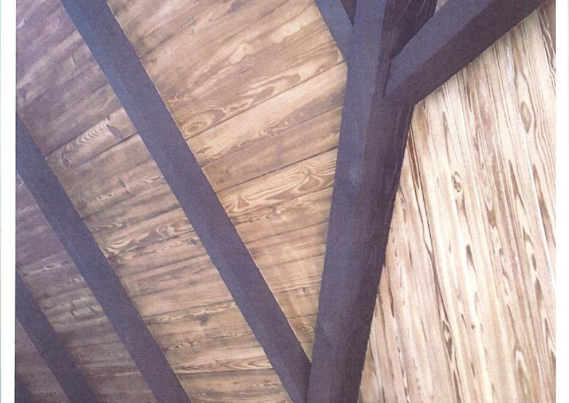 Close-up of a wooden ceiling with dark exposed beams and pale woven paneling.