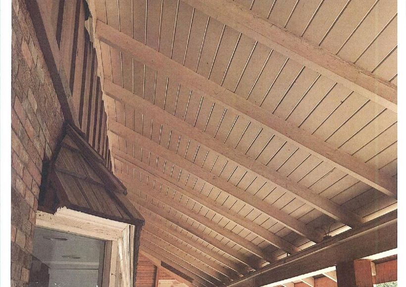 Wooden porch ceiling with exposed beams and slatted planks above a doorway