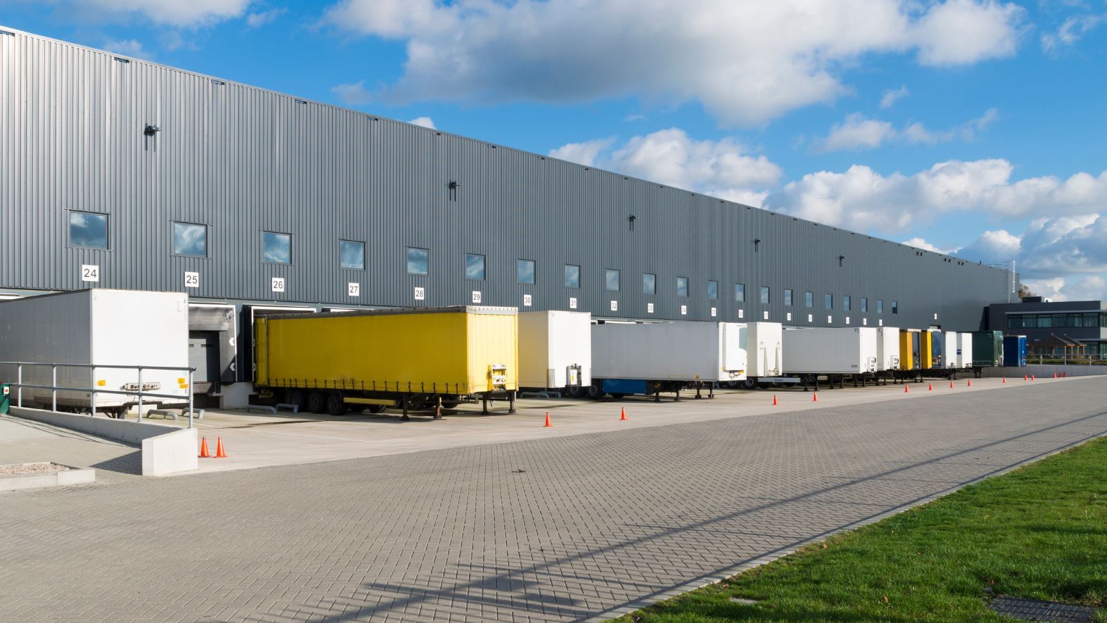 Industrial warehouse loading docks with yellow trailers and parked trucks under a blue sky