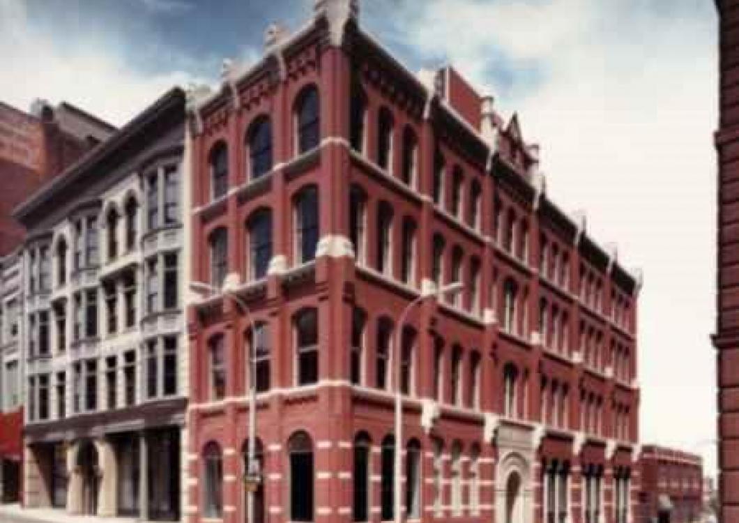 Red-brick historic corner building with arched windows and ornate trim in an urban street scene