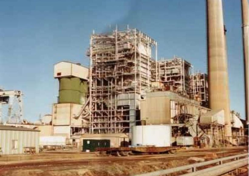 Industrial plant with scaffolding, smokestacks, and tanks in a dusty outdoor setting