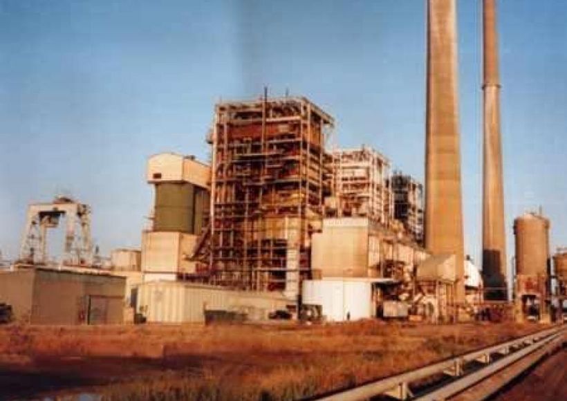 Industrial factory with smokestacks and scaffolding beside railway tracks under a clear sky