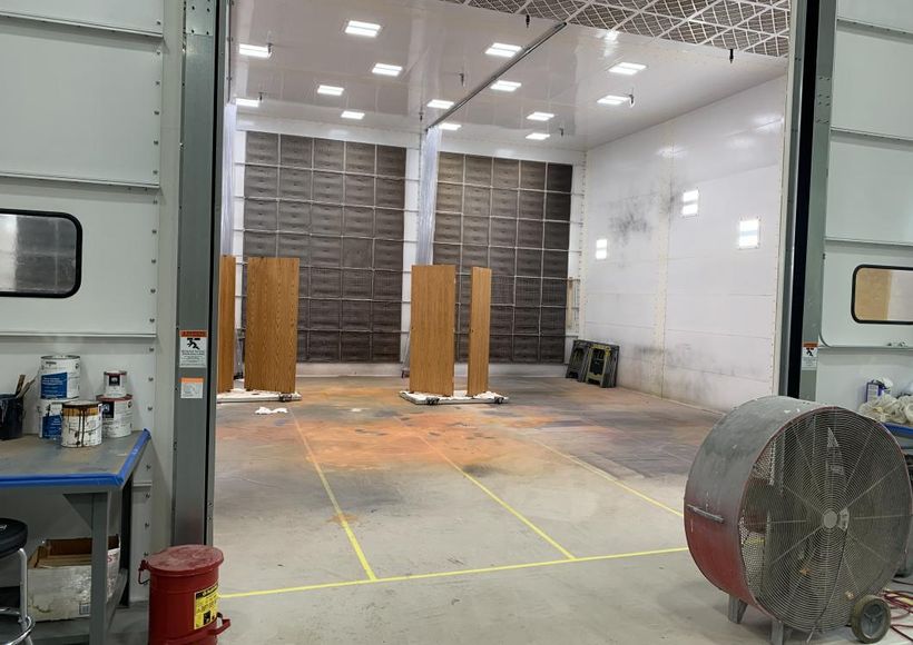 Empty industrial room with white walls, concrete floor, and open overhead door; equipment and tables at sides