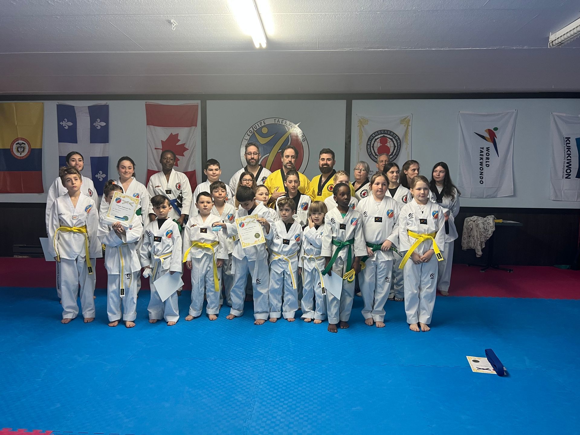 Deux pratiquants d'arts martiaux s'entraînent au combat sur des tapis bleus et rouges dans une salle de sport, levant les mains pour bloquer ou frapper.