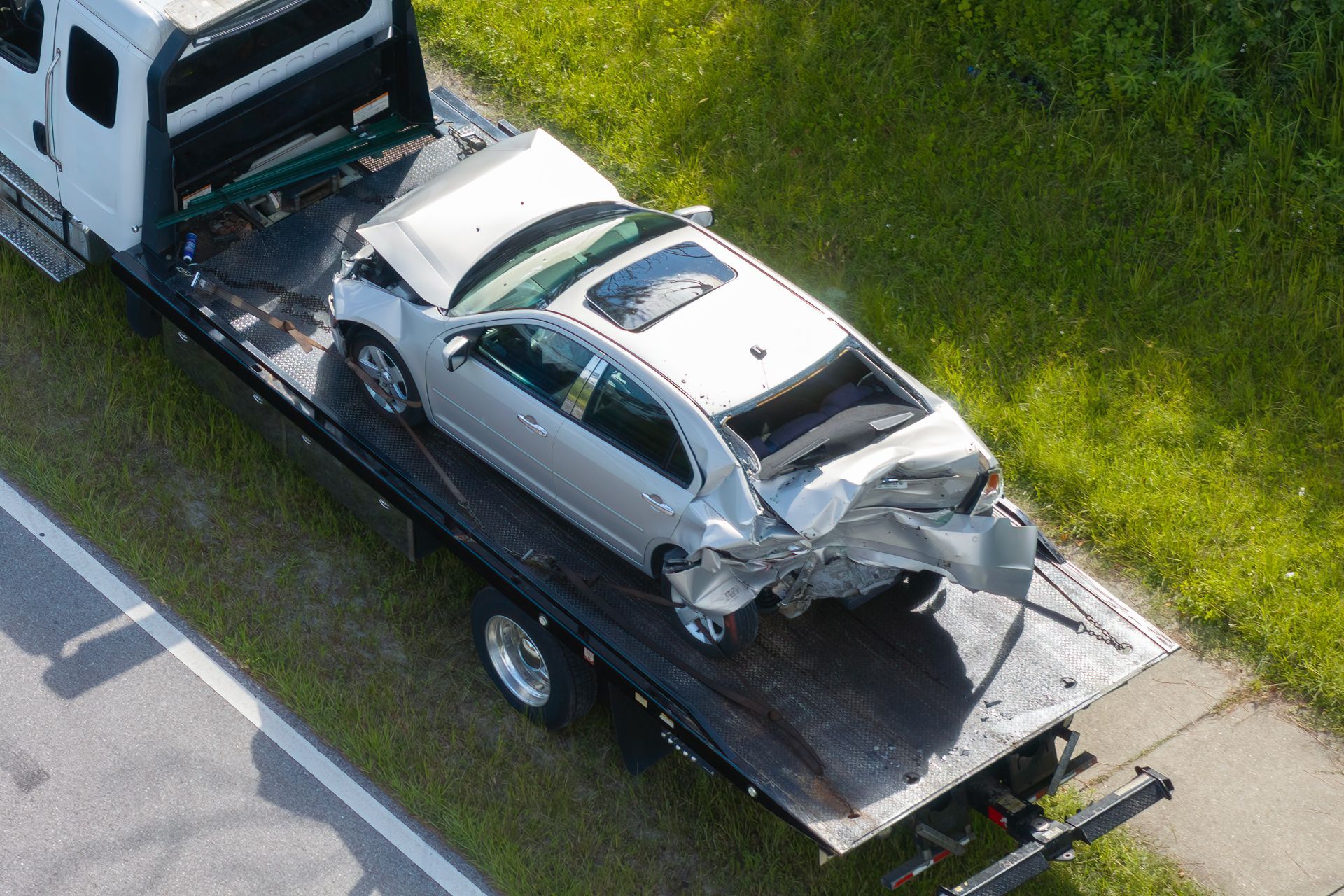 Silver car severely damaged on a tow truck, likely after an accident.