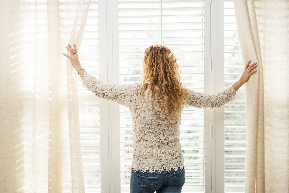 Woman Is Opening Her Curtains And Looking On A Window — Ezi Slide - Glass, Sliding, Track & Security Doors Repair in Ashmore, QLD