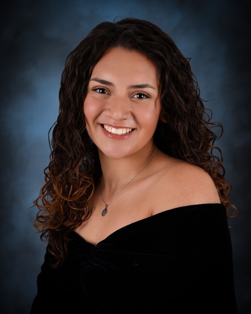 A woman with long curly hair is wearing a black off the shoulder top.