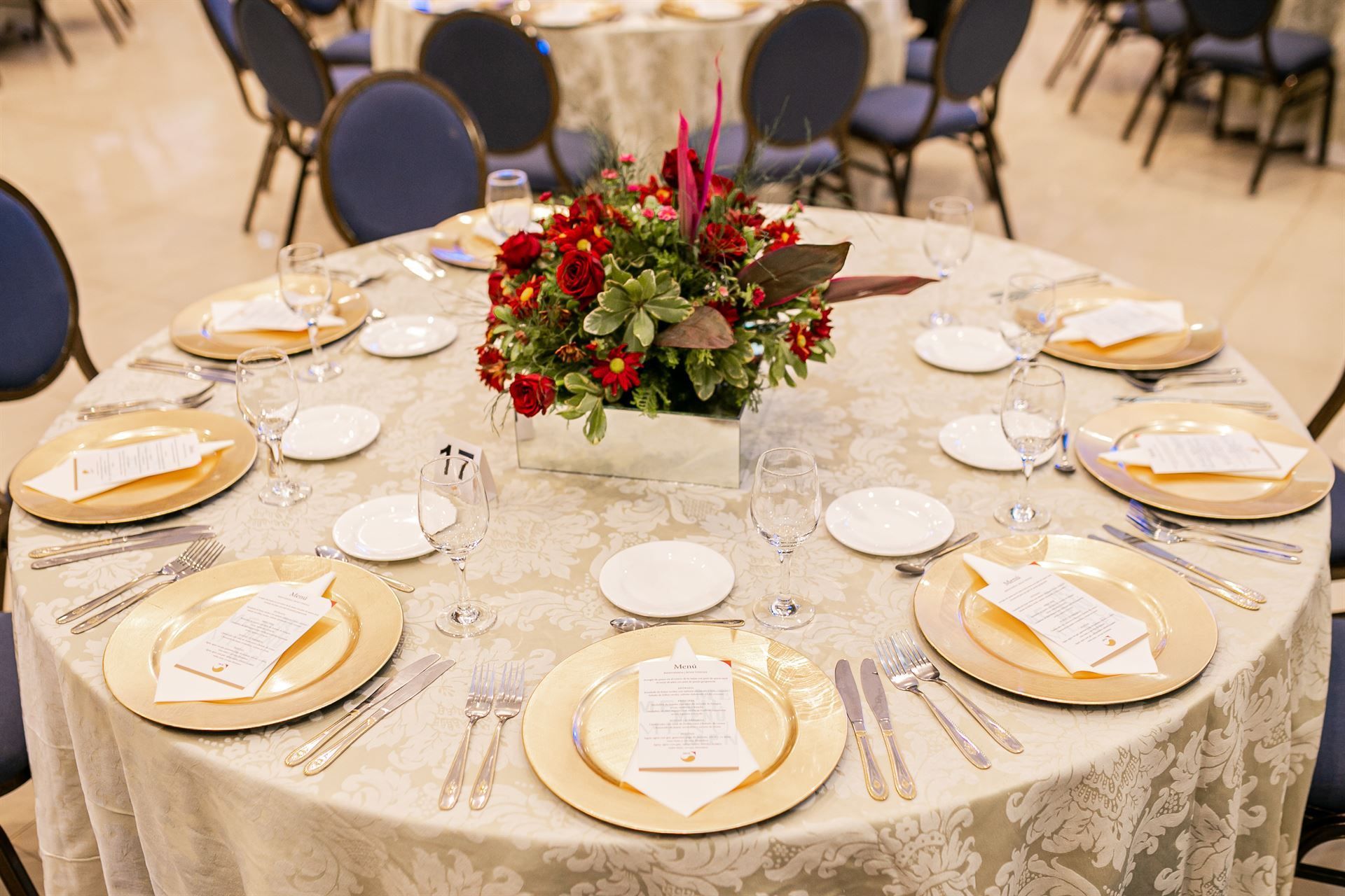 Una mesa redonda con platos, cubiertos y un jarrón con flores sobre ella.