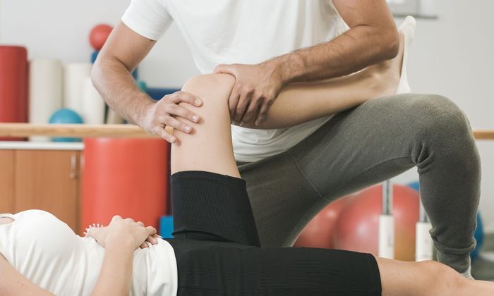 A man is stretching a woman 's leg in a gym.