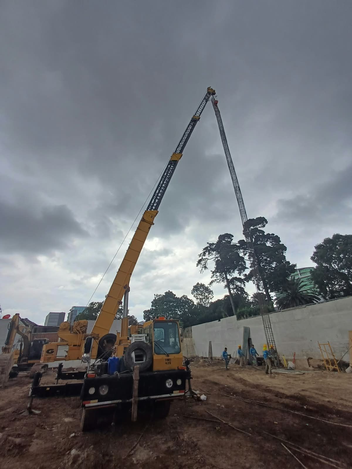 Dos grúas azules levantan un gran tanque cilíndrico en una obra de construcción.