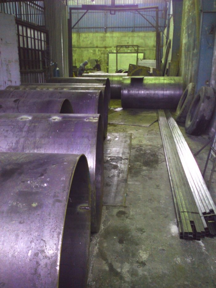 Taller industrial con grandes tuberías y vigas de metal morado apiladas sobre un suelo de hormigón.