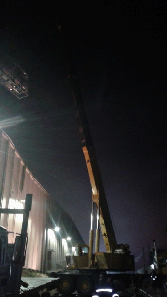 Equipo de elevación de grúa junto a un gran edificio por la noche.