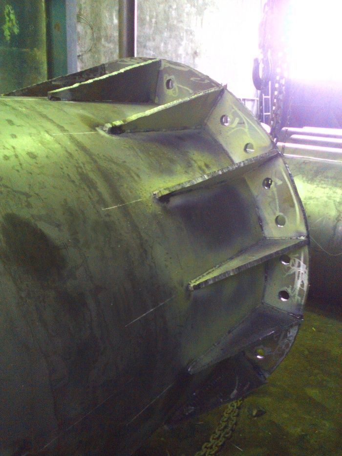 Tambor industrial verde con aletas y pernos metálicos en un entorno de taller.