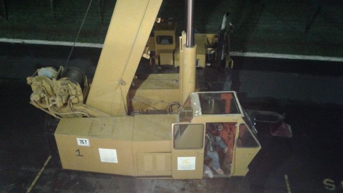 Gran máquina industrial amarilla en un almacén oscuro, con una cabina de control roja y material enrollado a la izquierda.