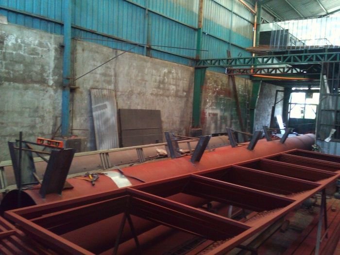 Taller industrial con una gran estructura metálica roja y equipo de soldadura dentro de un edificio de fábrica.