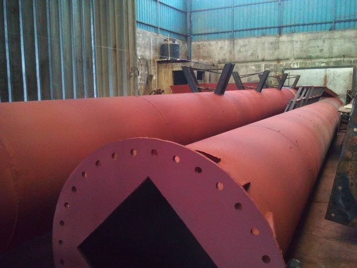 Grandes tuberías industriales rojas en un entorno que recuerda a una fábrica, con extremos bridados y soportes metálicos.