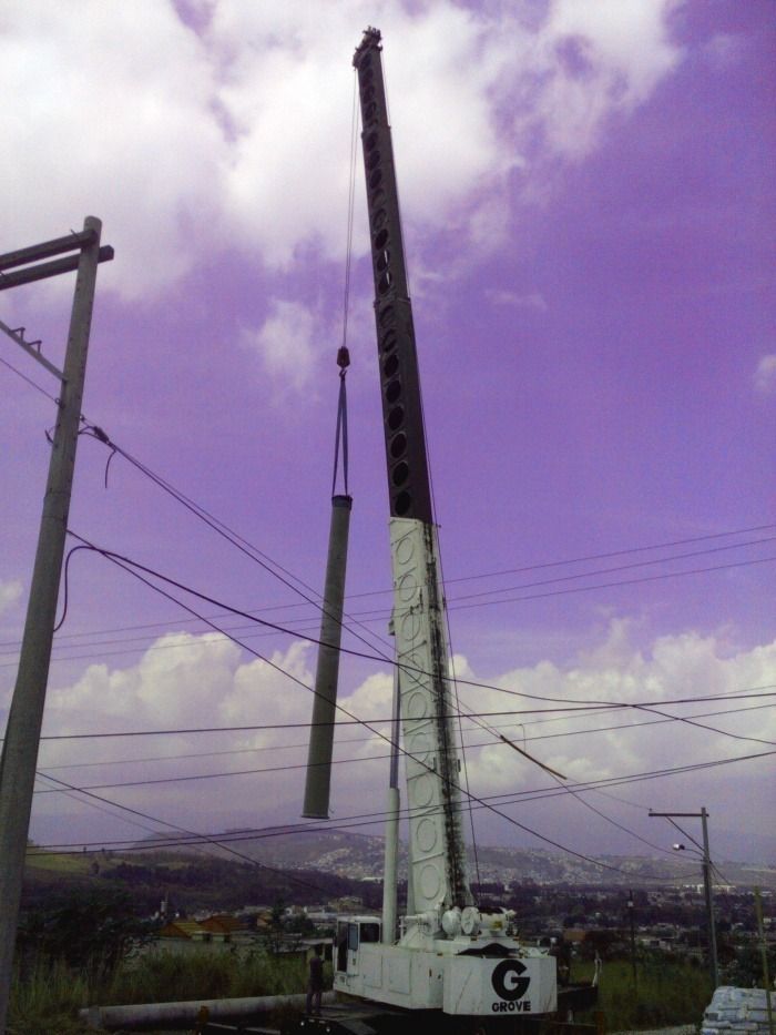 Una grúa levanta una larga viga de metal contra un cielo púrpura sobre un paisaje urbano.