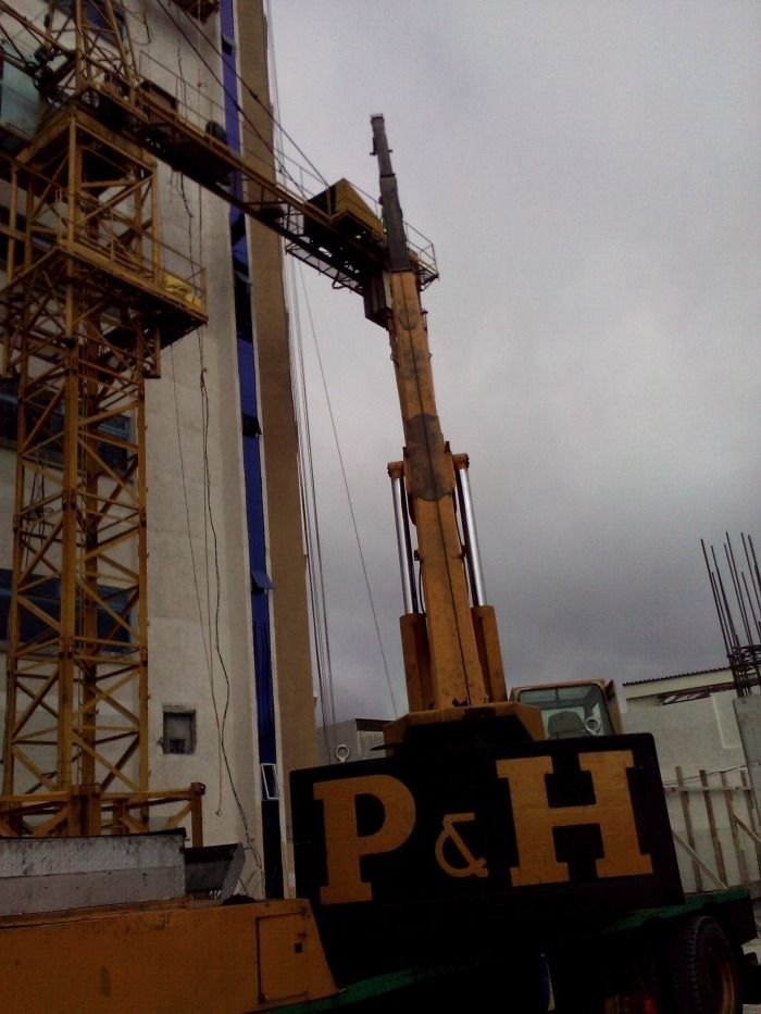 Grúa de construcción junto a una torre bajo un cielo nublado, con una máquina P&H en primer plano.