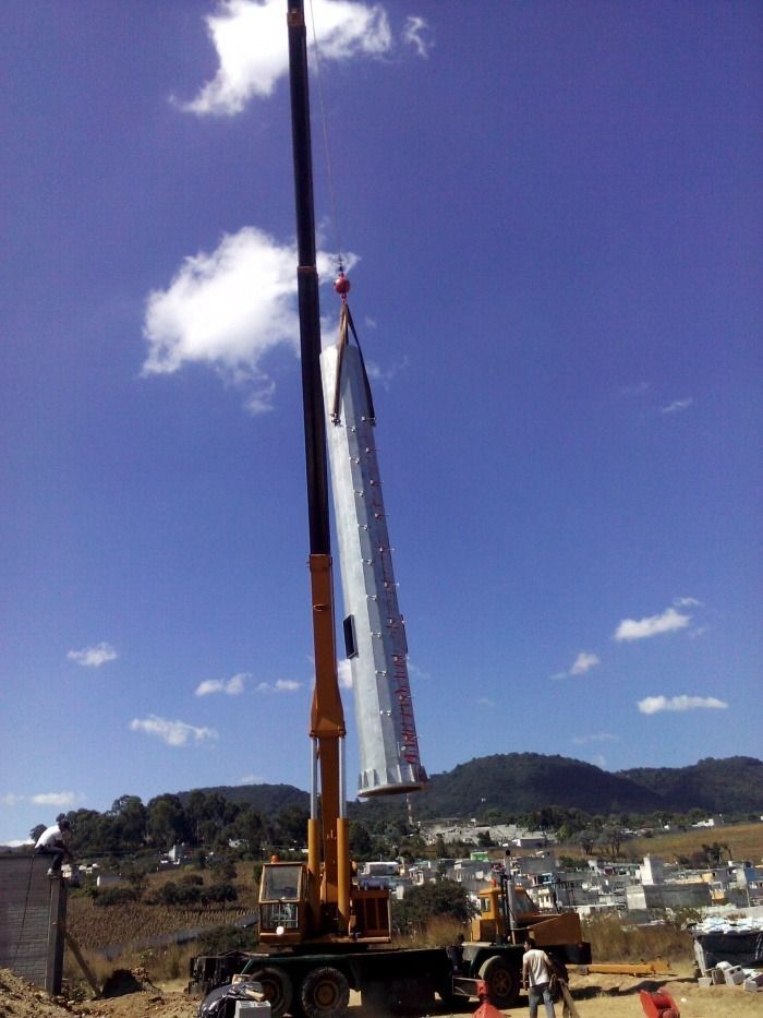 Una grúa levanta una larga viga metálica en una obra de construcción bajo un cielo azul.