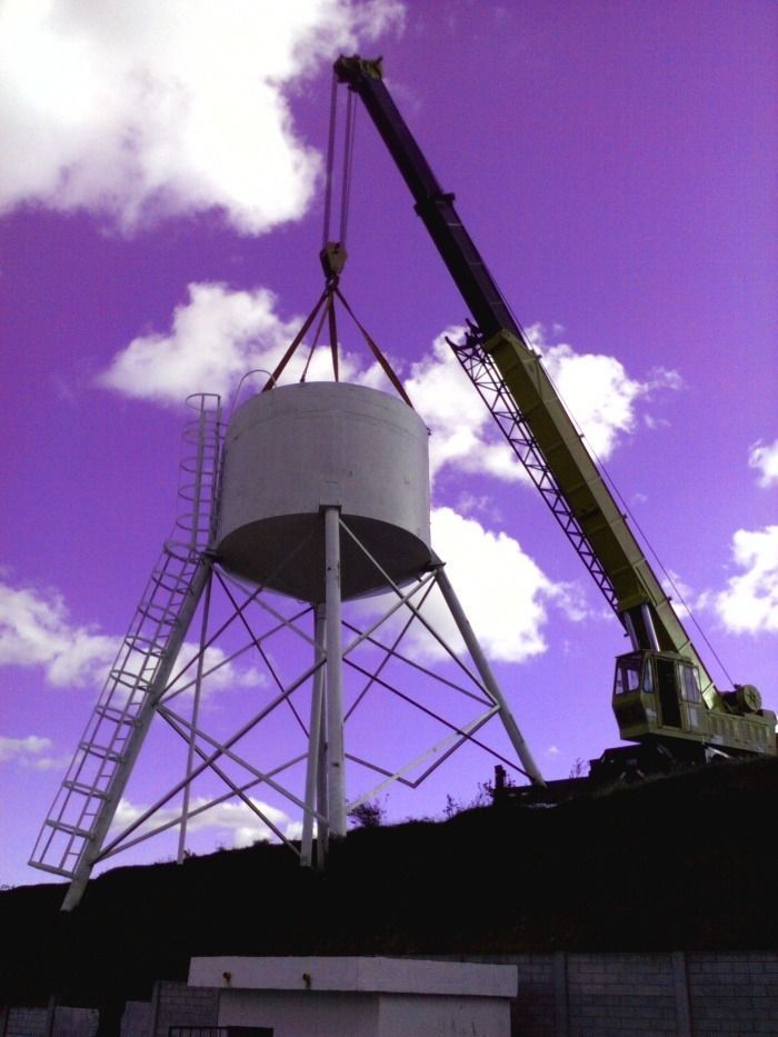 Grúa levantando la estructura blanca de un tanque de agua contra un cielo púrpura