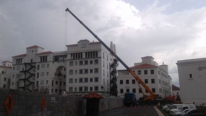 Calle urbana con edificios de apartamentos blancos y una grúa larga e inclinada contra un cielo nublado.