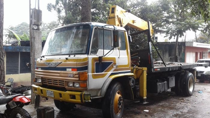 Camión grúa amarillo estacionado en una calle mojada junto a un poste de servicios públicos y edificios.