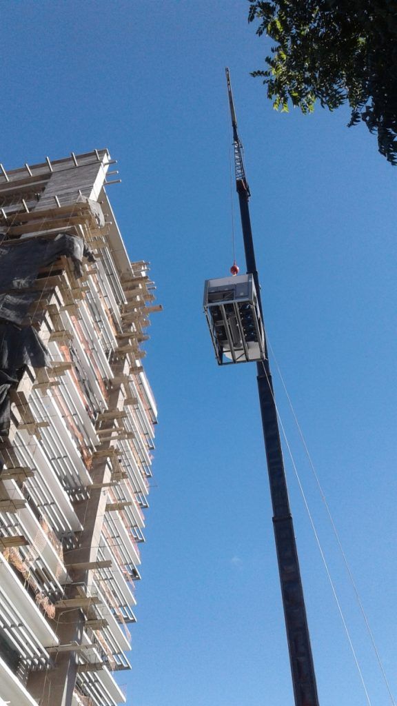 Grúa de construcción alta junto a un rascacielos beige contra un cielo azul claro