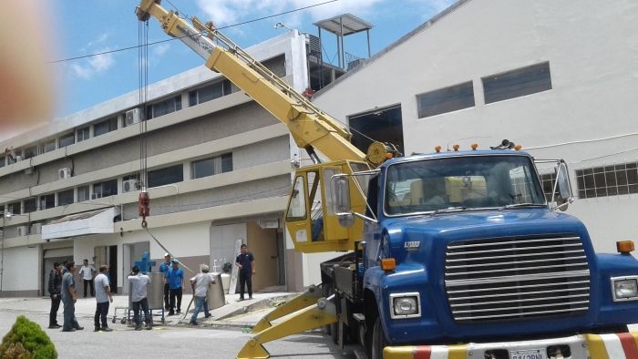 Una grúa azul levanta una cesta de trabajo junto a un edificio blanco con gente reunida debajo.