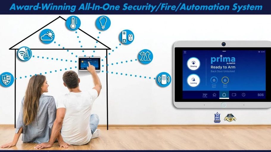 Two people sit on the floor facing a wall-mounted home security control screen with smart home icons above them.